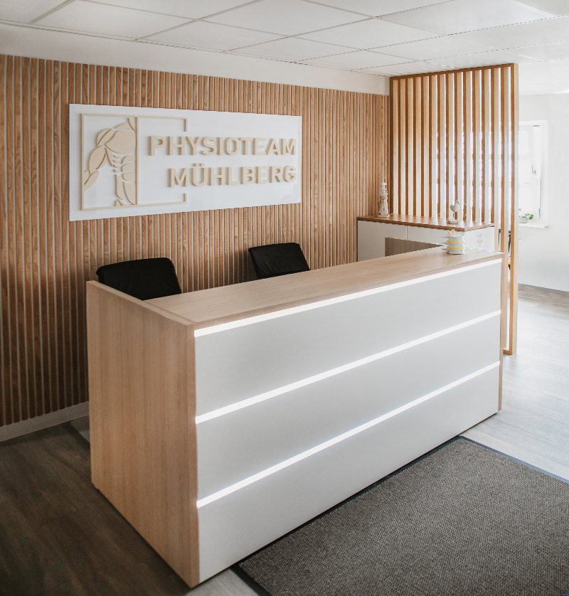 Empfangsbereich der Praxis Südstadt mit Physioteam Mühlberg Logo an der Holzwand